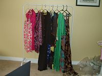Photo of 10 dresses hanging on white metal rack against a beige wall showing variety of colors and styles.