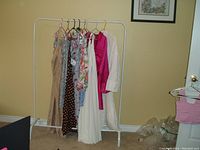 Photo showing nine ZARA dresses on a white garment rack in a room with beige walls, various styles including beige satin, floral, polka dot, pink, white pleated, and more.