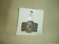 Photo showing silver colour cuff bracelet with intricate filigree design and attached tag indicating it is new.