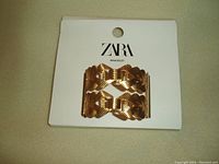 Photo of a gold colour cuff bracelet from ZARA displayed on a white branded card, showing the front side with the bracelet and the brand name on the card.