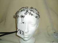 Front view of black hair band with clear crystal floral pattern displayed on white mannequin head with ZARA tag attached.