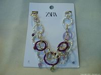 Photo of ZARA necklace on branded card featuring linked pearls, purple and gold rings.