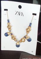 Front view of ZARA necklace showing blue teardrop stones and gold textured beads on gold chain, on original branded card with tag.