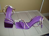 Front-side view of purple ankle wrap heeled sandals showing straps, heel height, and attached tags.