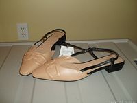 Side angled view of a pair of tan ZARA slides with pointed toes and slingback black straps, shown with original tags attached on a tiled floor.
