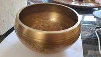 Side angle of solid brass singing bowl showing intricate interior engravings and exterior smoothness.