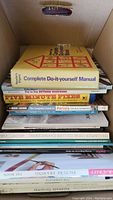 Top view of stacked do it yourself books inside a cardboard box, showing titles and covers.