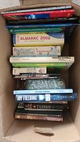 Box containing a variety of books including novels, almanac, toddler guide, and team building games books.