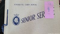 Front cover of the cigarette card album titled Senior Service with a ship logo and blue text.