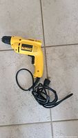 Full view of the yellow DeWalt electric drill with black power cord on tile floor.