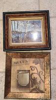 Photo shows the two framed art pieces laid on a tiled floor. The top frame contains a coffee cup mocha themed print with floral designs and lettering. The bottom frame contains a landscape of birch trees by a lake.