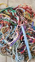 Top view of a large pile of assorted colorful beaded necklaces with mixtures of pastel and bright beads alongside some gold-tone chain accents