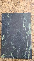 Top view of rectangular marble pastry board with green and black veining on a granite countertop.
