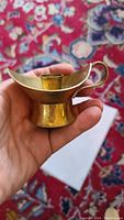 Hand-held solid brass magic lamp shaped candle holder showing front view with cylindrical candle cup and curved spout.