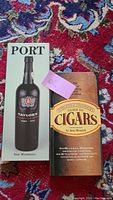 Two hardcover books, 'Port' by Neil Matthews featuring a bottle of Taylor's Port on the cover, and 'The Connoisseur's Guide to Cigars' by Jane Merrick with a brown and orange cover. Book titles and authors clearly visible.