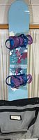 Full length view of Burton Feather 39+ snowboard with purple and blue bindings and black carry bag