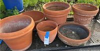 Six large terracotta clay pots of varying sizes on metal shelf outdoors, showing natural weathering and dirt residues.