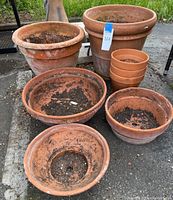 Photo showing six clay pots grouped together on paved surface, some stacked. Pots show dirt residue, weathering and wear consistent with outdoor use.