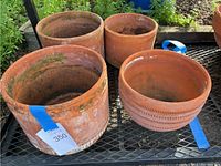 Four medium terracotta clay pots outdoors on metal grid surface showing weathering and moss.