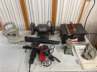 Full view of all tools showing bench grinder, table saw, angle grinder, and leaf blower laid out on table