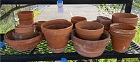Wide shot showing a collection of terra-cotta pots arranged on a metal shelf, varying in sizes and showing signs of wear and weathering.