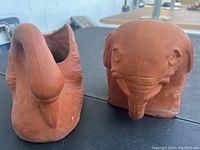 Both terra-cotta planters, a swan and an elephant, shown side by side on a table to display overall shapes and sizes.