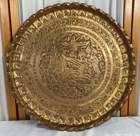 Full view of circular brass tray showing scalloped edge and central engraved scene