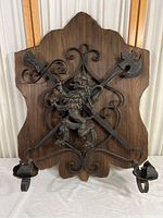 Full view of the wood plaque with wrought iron lion and crossed weapons candle holder.