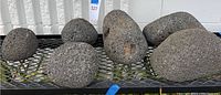 Wide angle photo showing six volcanic rocks of various sizes on a black metal mesh surface.
