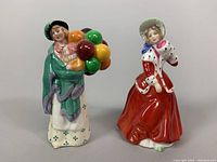 Front view of both Royal Doulton figurines, showing "The Balloon Seller" holding balloons and "Christmas Morn" in red dress.