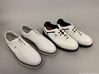 Two pairs of men's golf shoes: one FootJoy pair in white leather and one Callaway pair in white with black trim.