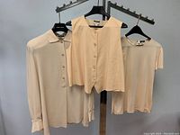 Full view of three beige silk tops on hangers showing sleeveless vest, long sleeve blouse, and short sleeve top