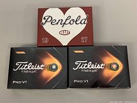 Photo of two open boxes of Titleist Pro V1 golf balls and one Penfold Heart golf balls box on top.