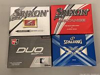 Four open boxes of golf balls: Srixon Z-Star XV (white/gold box), Srixon Distance (red box), Wilson Staff Duo Soft+ (silver/black box), Spalding Tour Comp Super VX (blue/white box) arranged on table