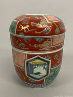 Side view of hand painted porcelain covered two-piece stackable bowl showing detailed dragon, floral motifs, and nature panels on red background.