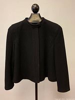 Front view of black wool jacket on hanger showing high collar and textured fabric