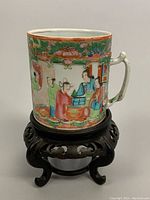 Front view of hand painted Rose Medallion mug on wooden base showing seated figures and floral border