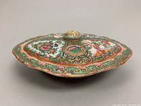 Side angle of covered serving dish showcasing its oval shape and detailed painted decoration with knob lid.