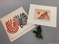 Photo of the Cape Dorset 1973 calendar, the small green soapstone eagle sculpture, and the signed 'Morning Sun' print.
