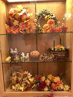Two shelves of autumn wreaths, flower bouquets, and Halloween-themed figurines including ghost figures and pumpkins