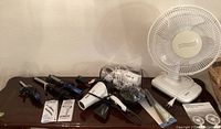 Photo showing three Conair curling irons, a white Conair hair dryer, a small white table fan, and digital scales on a wooden table.