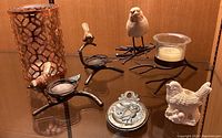 Bird-themed decor items displayed including metal bird candle holders, ceramic bird, metal medallion, patterned lantern, and decorative stones