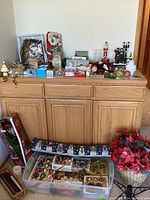 Wide view of large lot on wooden cabinet showing various Christmas decorations including boxes of globe ornaments, poinsettia flowers, and figurines.