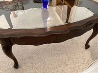 Close-up view of coffee table's dark wood ruffle trim and leg design under glass top.