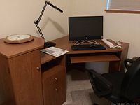 Corner desk with keyboard, clock, lamp, chair and clear chair pad, viewed from an angle.