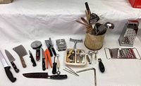 Wide view of all kitchen utensils laid out including knives, graters, wooden spoons, ladles, and various prep tools