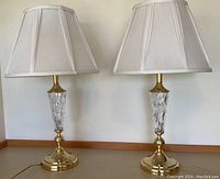 Pair of matching table lamps showing brass bases and cut glass bodies with white fabric lampshades.
