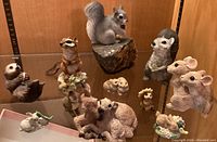 Multiple ceramic meadow animal figurines including squirrel on rock, chipmunks, rabbits, and deer in a wooden display case.