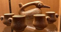 Photo showing the full view of the brown ceramic duck teapot with 4 matching cups each having duckling head handles and markings.