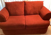 Front-facing view of solid red two-seat corduroy couch with plush cushions and rounded armrests.